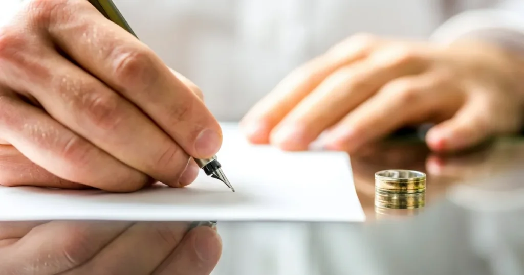 hands signing contested vs uncontested divorce with a ring sitting on the table